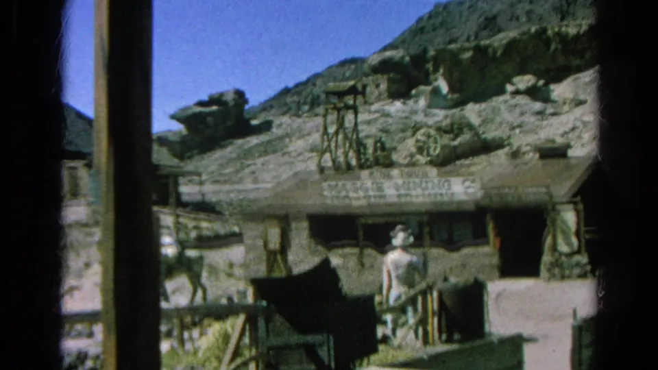 A person in a white hat walks near a rustic building marked Maggie Mining Co. in the 1966 Silver Lake home-movie footage.