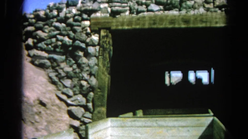 1966 8mm frame of a wooden train car approaching or entering a stone tunnel in a dry California hillside setting.
