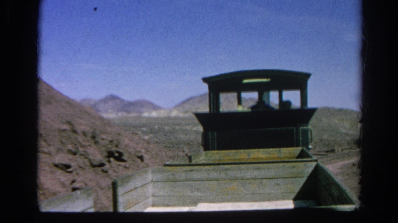 A small wooden train cab moves through arid hills near Silver Lake, California, with shadowed figures visible inside.