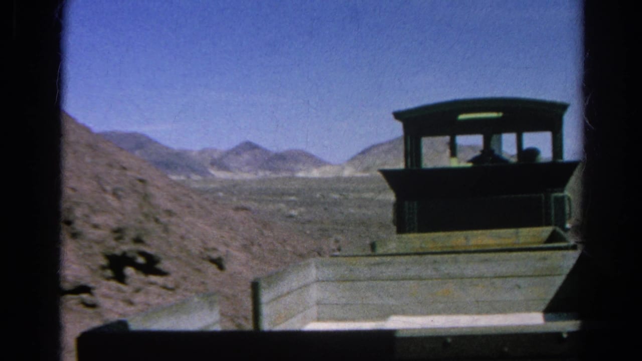 1966 home-movie frame showing a wooden train cab and car traveling through dry hills under a clear sky.