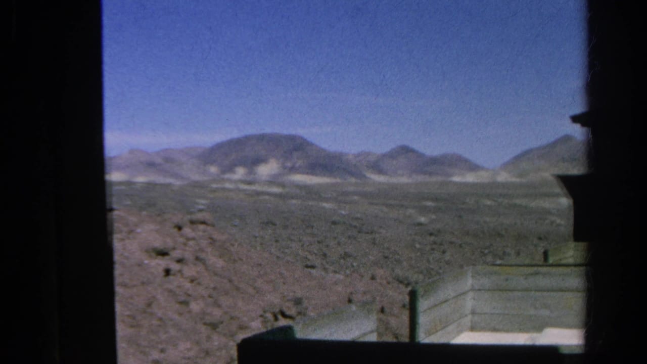 Arid landscape and distant hills framed by the side of a train.