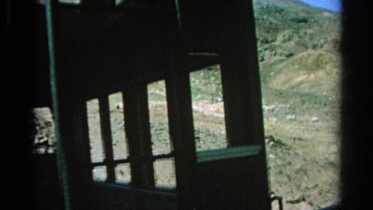 Dark train structure and multiple window openings frame a rocky Silver Lake desert hillside in this 1966 8mm still.