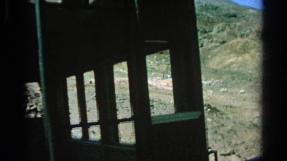 Dark train structure and multiple window openings frame a rocky Silver Lake desert hillside in this 1966 8mm still.