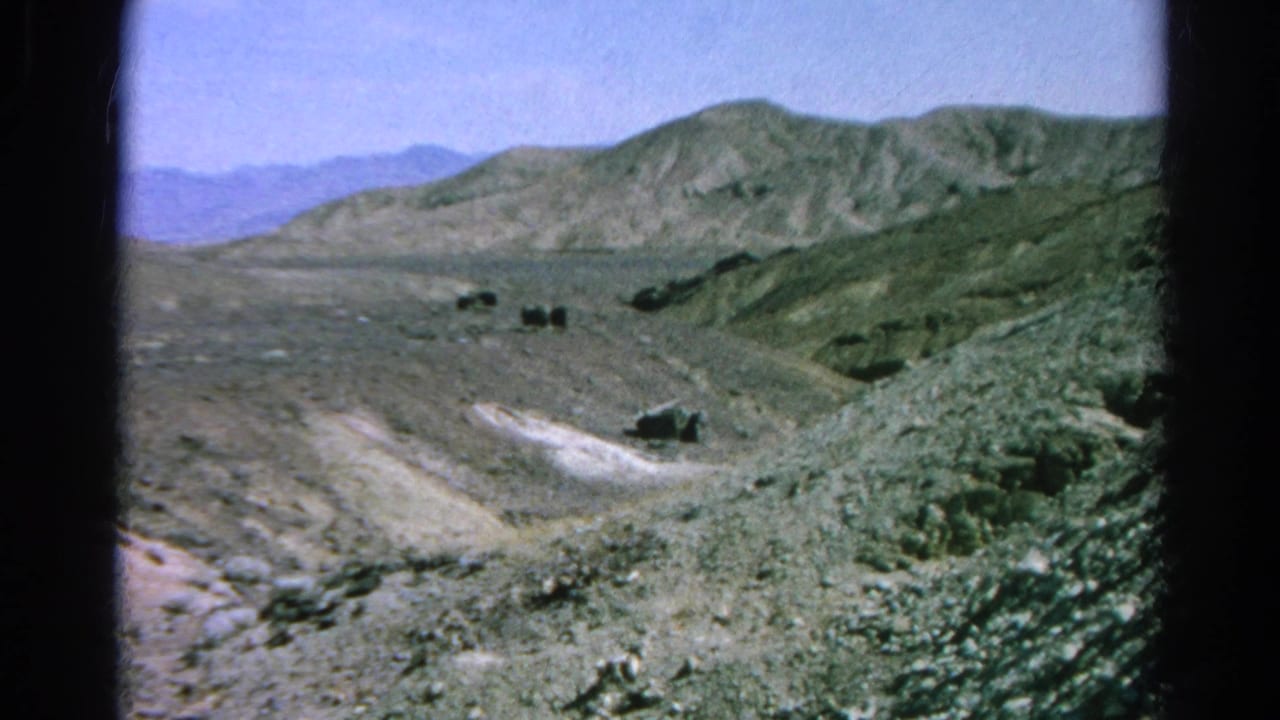 Wide dry valley with rocky hills, dirt tracks, and distant mountains.