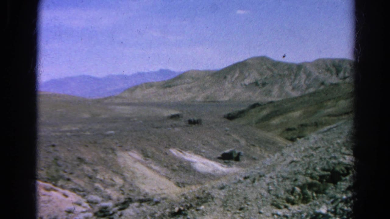 1966 8mm passenger view across a barren Silver Lake mountainside, with pale tracks, rocky slopes, and distant hills.