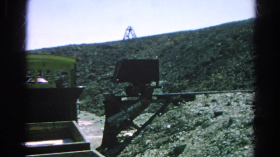 1966 8mm frame from Silver Lake showing the tram moving past a dark support structure on a rocky mountain grade.
