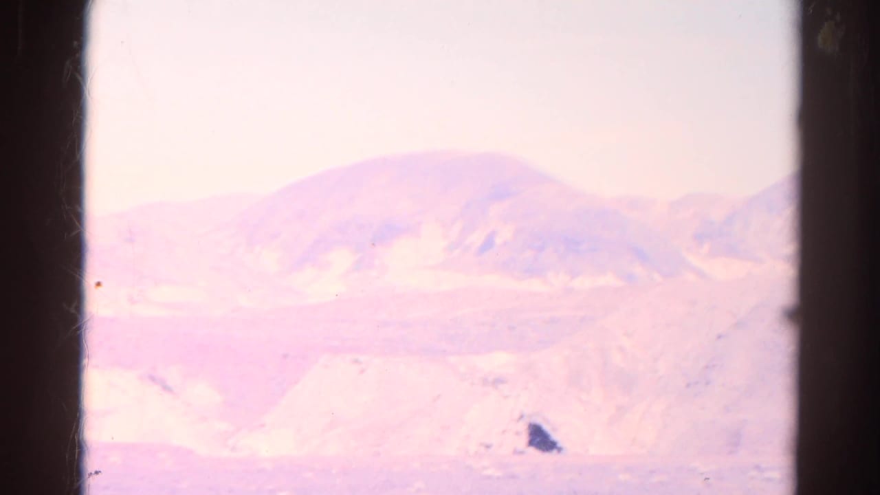 Pastel desert mountains and sand ridges seen through a dark window frame.