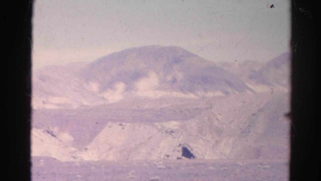 A faded 1966 8mm frame shows a distant mountain slope and sandy desert terrain divided by a dark window edge.