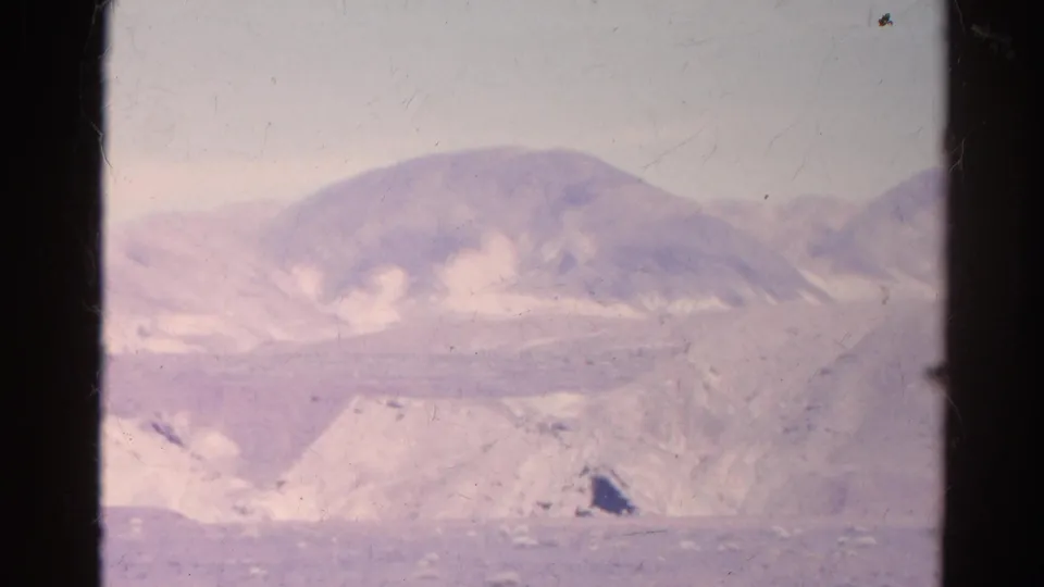 A faded 1966 8mm frame shows a distant mountain slope and sandy desert terrain divided by a dark window edge.
