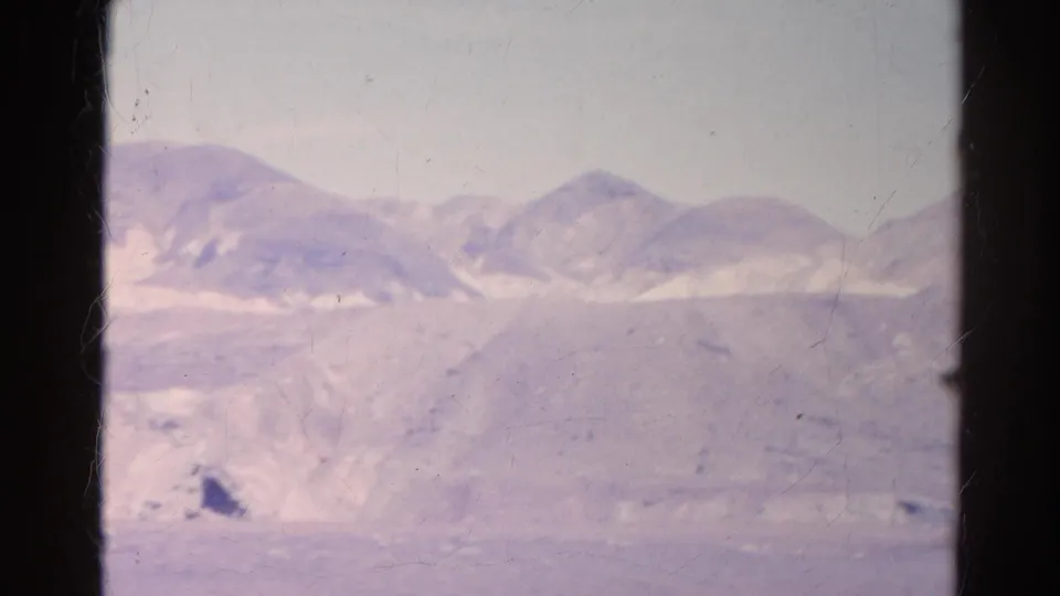 The 1966 home-movie frame shows low desert hills and sandy foreground through a dark-framed window opening.