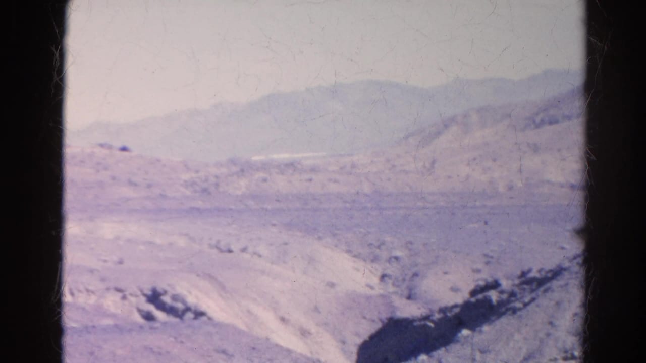 Distant rounded hills and dry ridged ground seen through a dark vertical film edge.