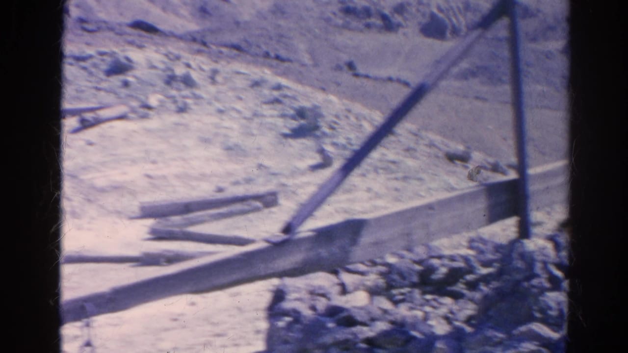 Dry ground with long planks, posts, rocks, and a low edge.
