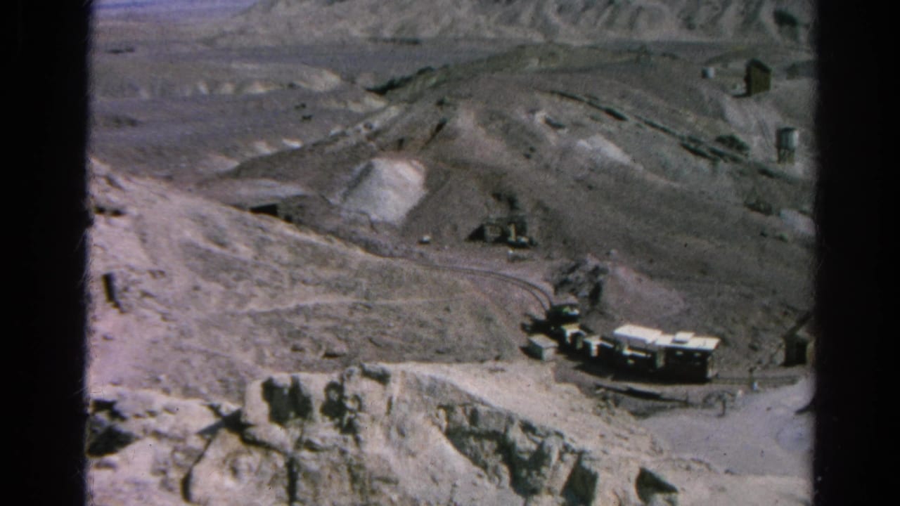 Large trucks on a narrow dirt road through a rocky mountain worksite.