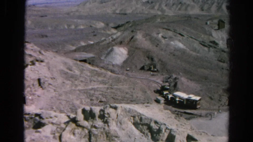 1966 Silver Lake, California 8mm frame with trucks near pale railcars or trailers in a rugged industrial landscape.