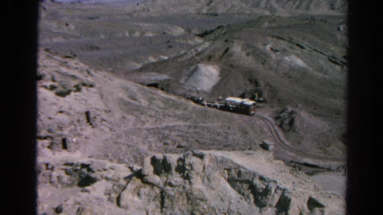 1966 Silver Lake, California 8mm frame showing trucks spaced along a curving dirt road in a barren mountain worksite.