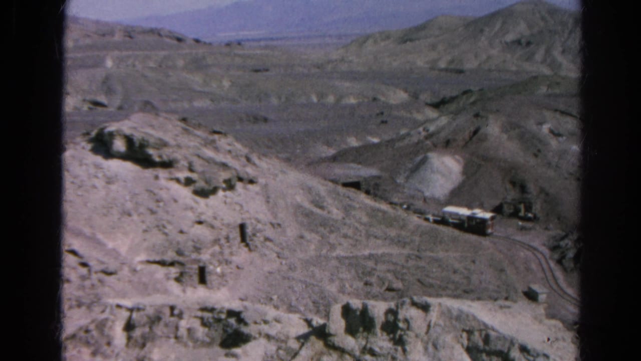 Desert hills with small vehicles on a winding dirt road.