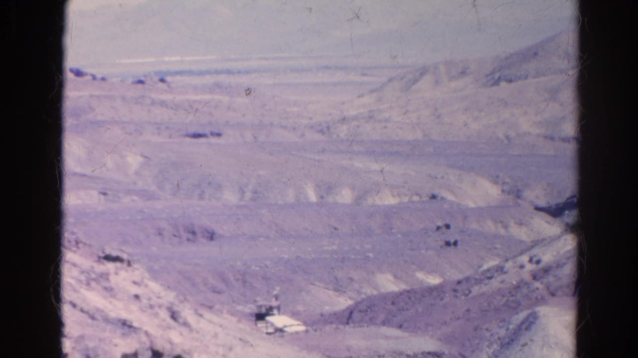 Wide 1966 Silver Lake desert view with pale ridges, distant mountains, and small indistinct vehicle or infrastructure shapes.