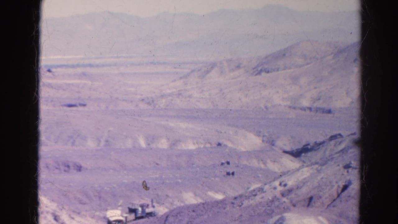 Wide desert landscape with a small train low in frame and mountains in haze.