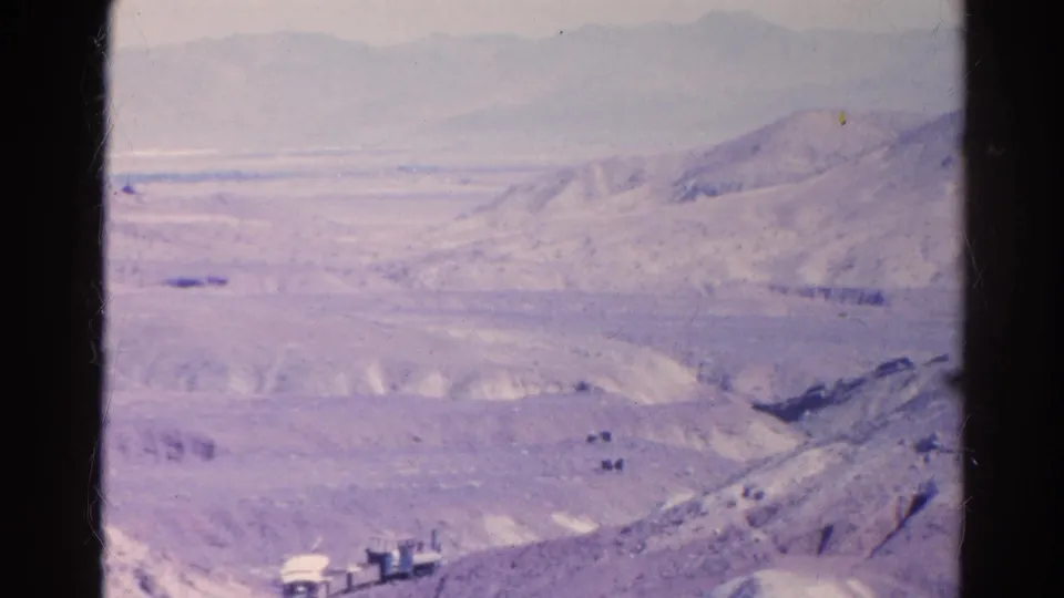 Faded 1966 home-movie frame showing a small rail vehicle below rolling desert hills and a hazy mountain backdrop near Silver Lake, California.