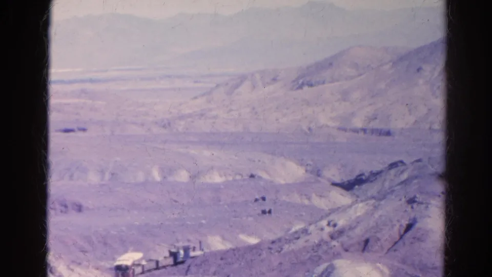 End frame of the 1966 8mm clip with a small train or rail vehicle at the lower edge, set against layered desert hills near Silver Lake, California.