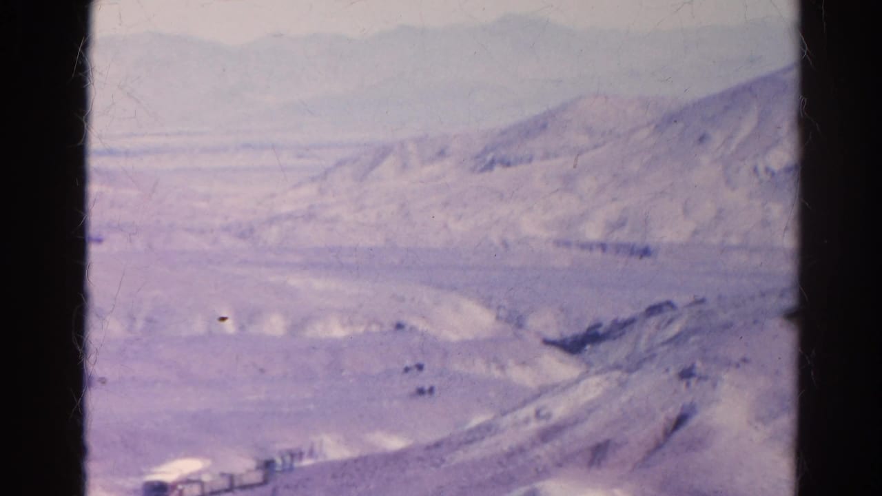 Hazy desert valley with pale hills and distant mountains seen through 8mm film edges.
