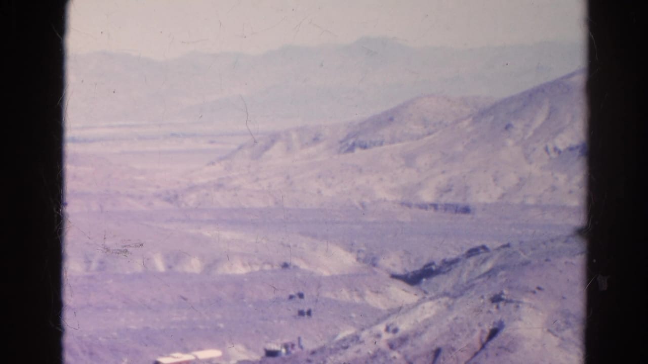 Wide view of pale arid mountains and valley roads through a dark film frame edge.