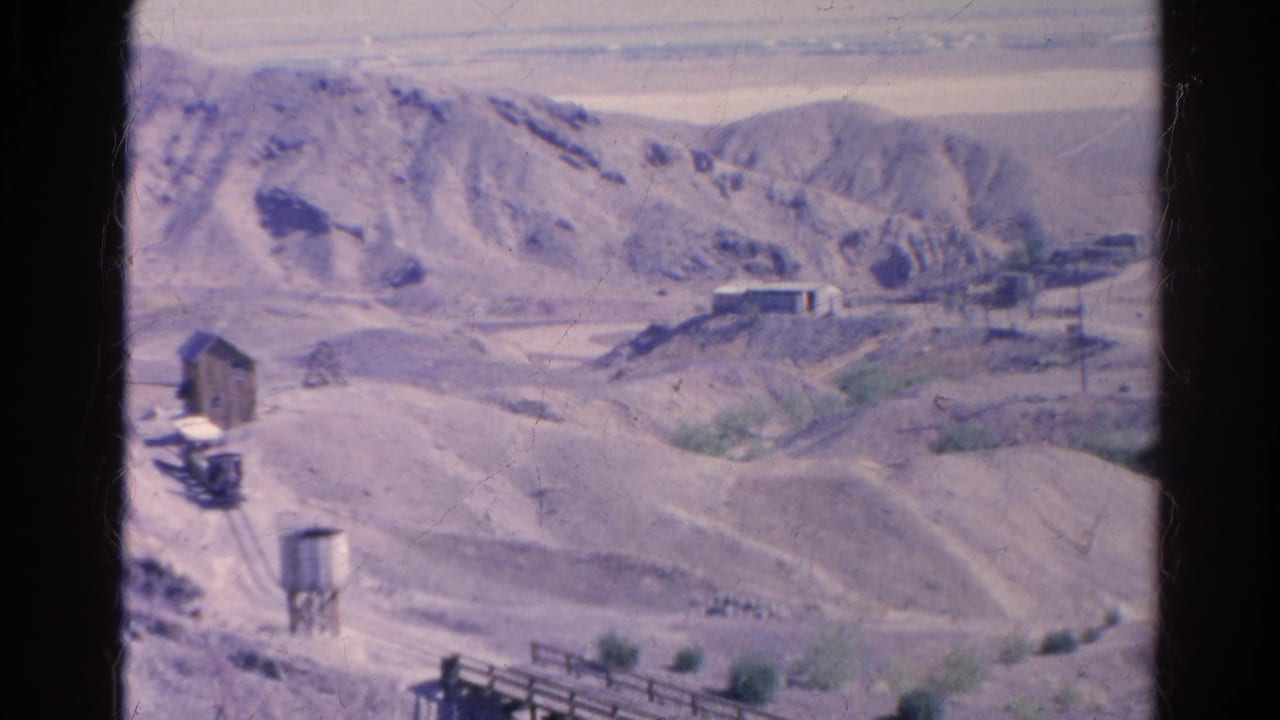 1966 Silver Lake, California desert mining landscape with pale hills, scattered structures, a water tower, rail lines, and a wooden trestle.