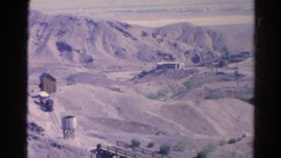 1966 Silver Lake, California desert mining landscape with pale hills, scattered structures, a water tower, rail lines, and a wooden trestle.