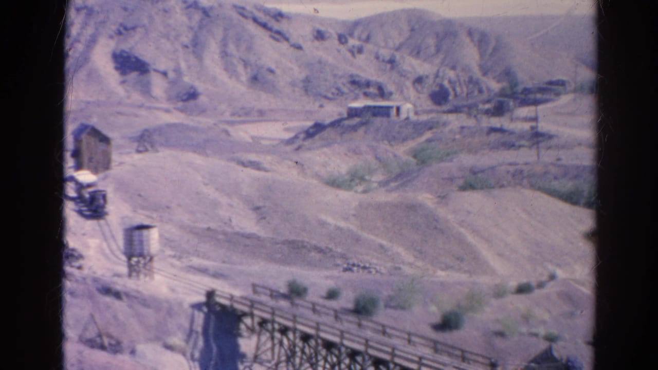 Barren hills, rail tracks, a water tower, small buildings, and a wooden bridge crossing the lower frame.