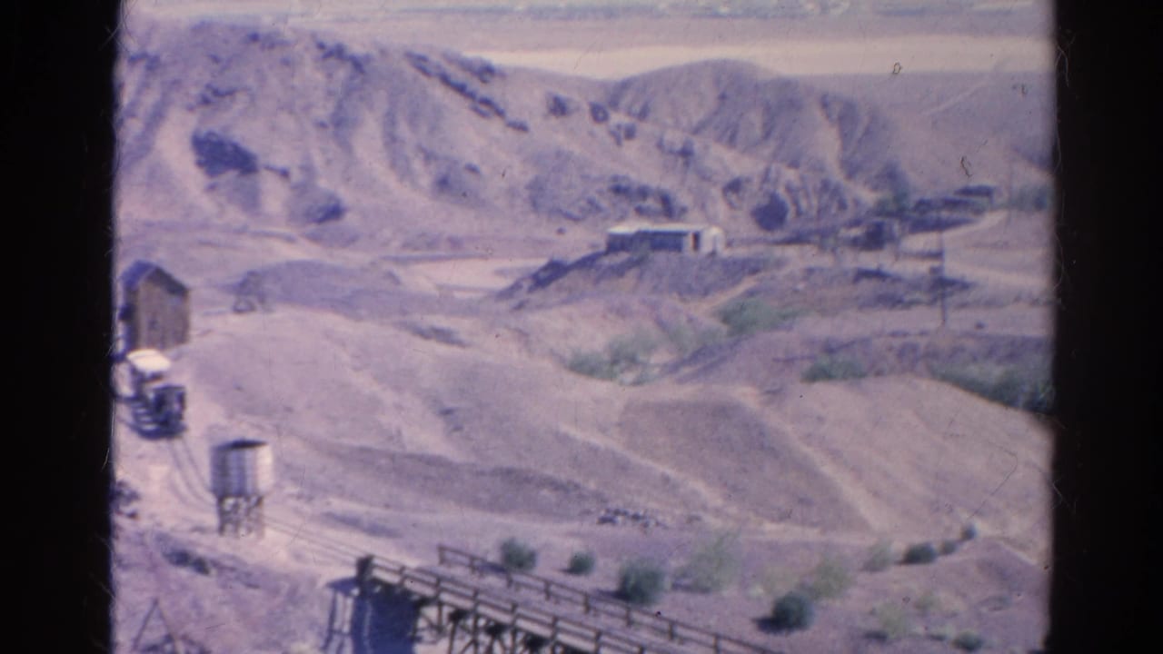 Aged 8mm frame from Silver Lake, California showing a sparse desert industrial scene with hills, rails, structures, and a trestle.