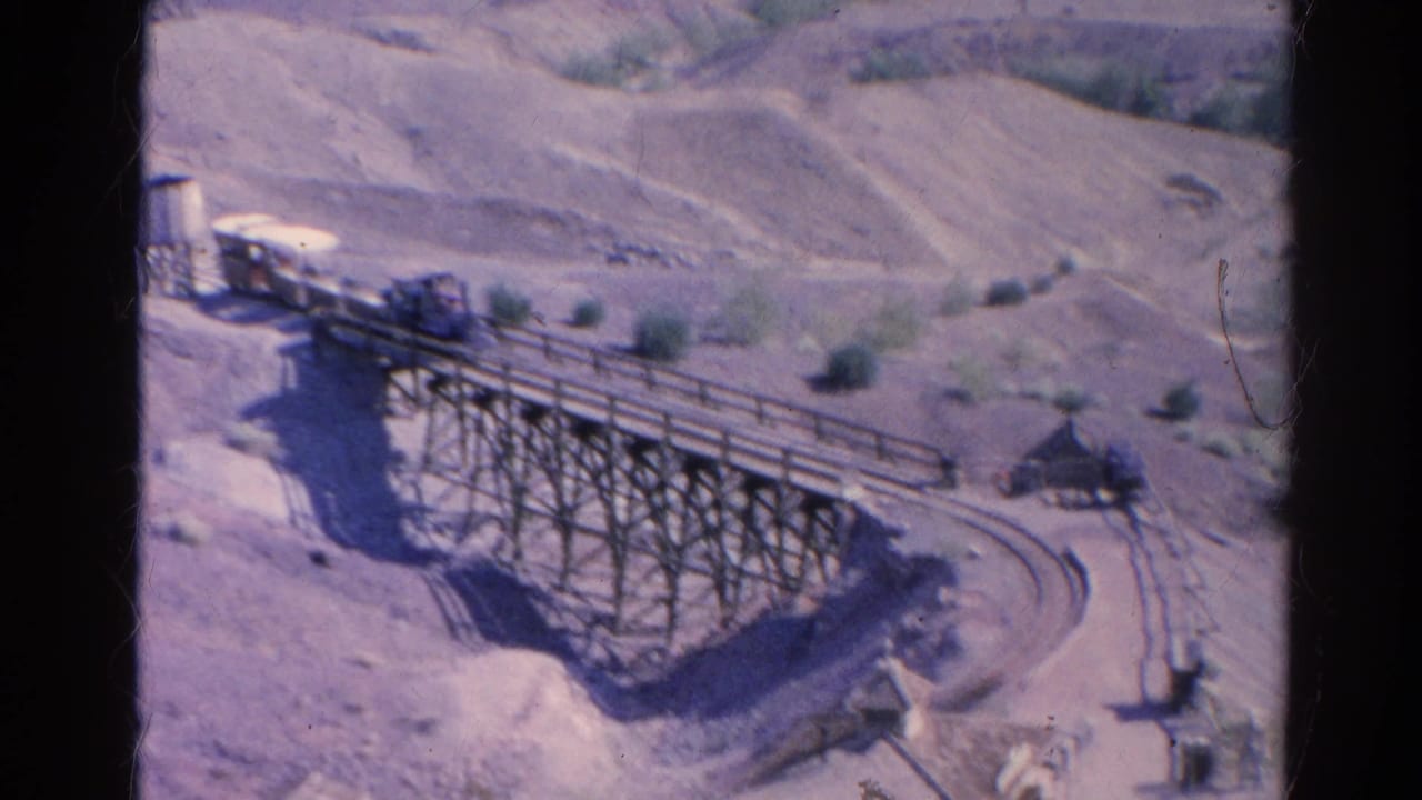 1966 Silver Lake 8mm frame with a small train moving across a wooden trestle bridge in a rugged desert landscape.