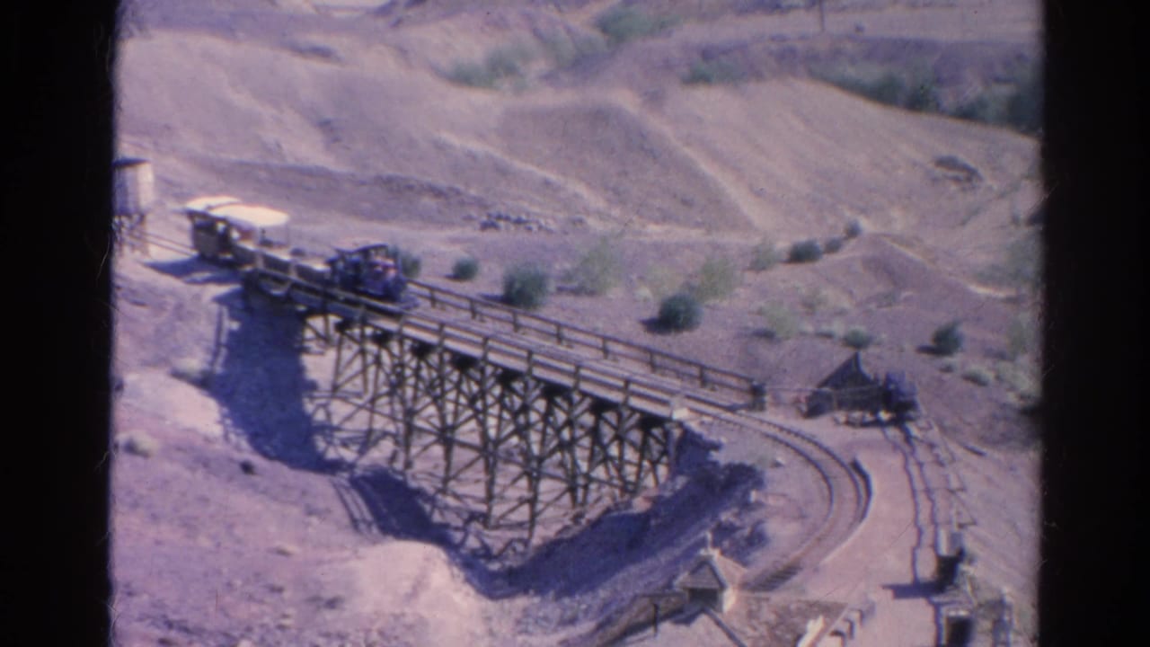 1966 home-movie frame from Silver Lake showing the train partway across the wooden trestle above dry terrain and curved rails.