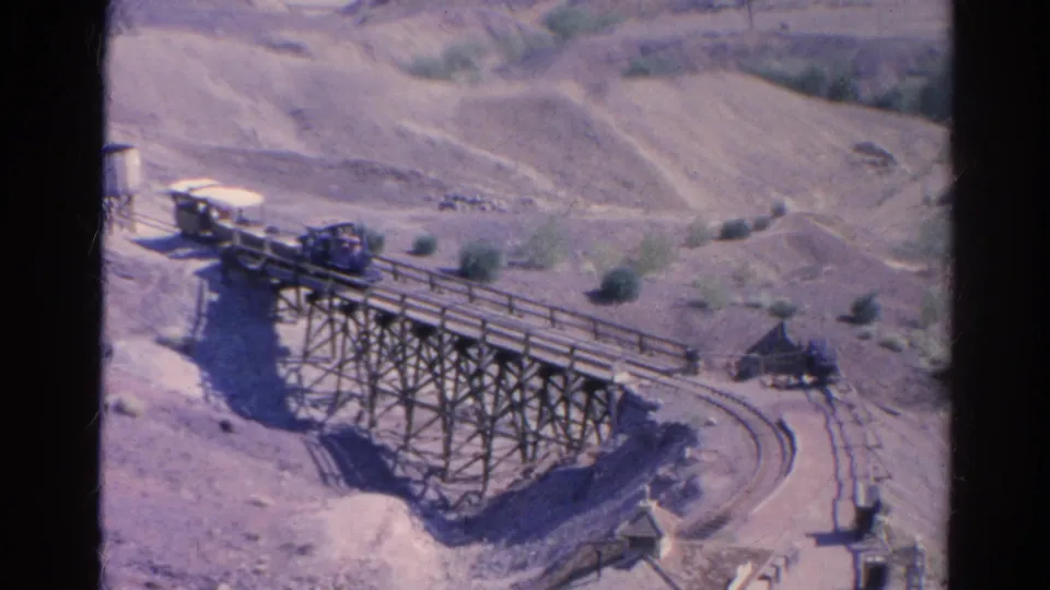 1966 home-movie frame from Silver Lake showing the train partway across the wooden trestle above dry terrain and curved rails.