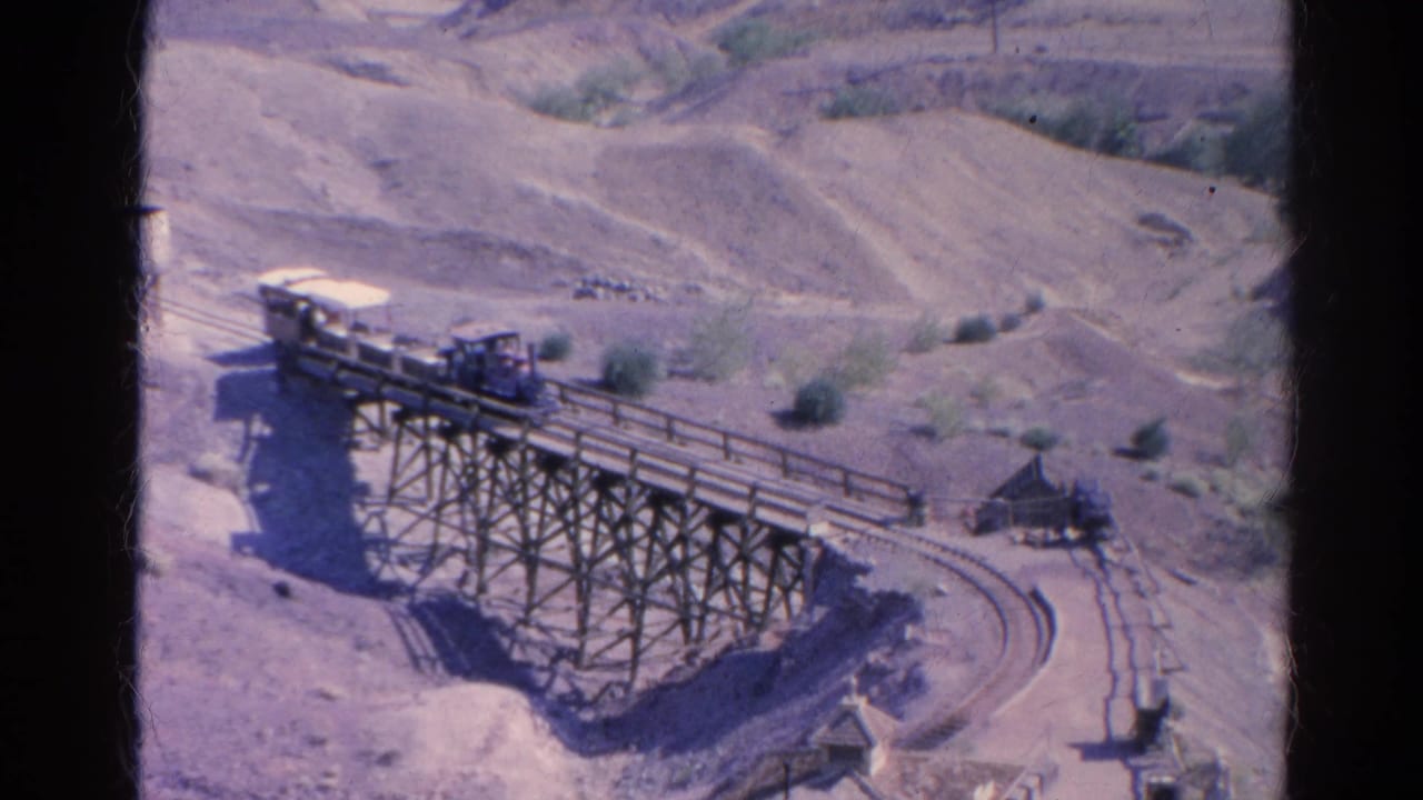 Small train crossing a wooden trestle bridge in dry hills.