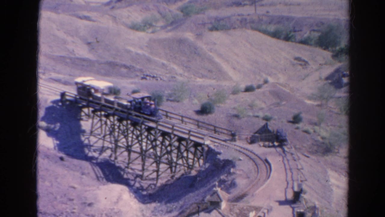 Small passenger train continues across the wooden trestle in 1966 Silver Lake, with scrubby hills behind it.