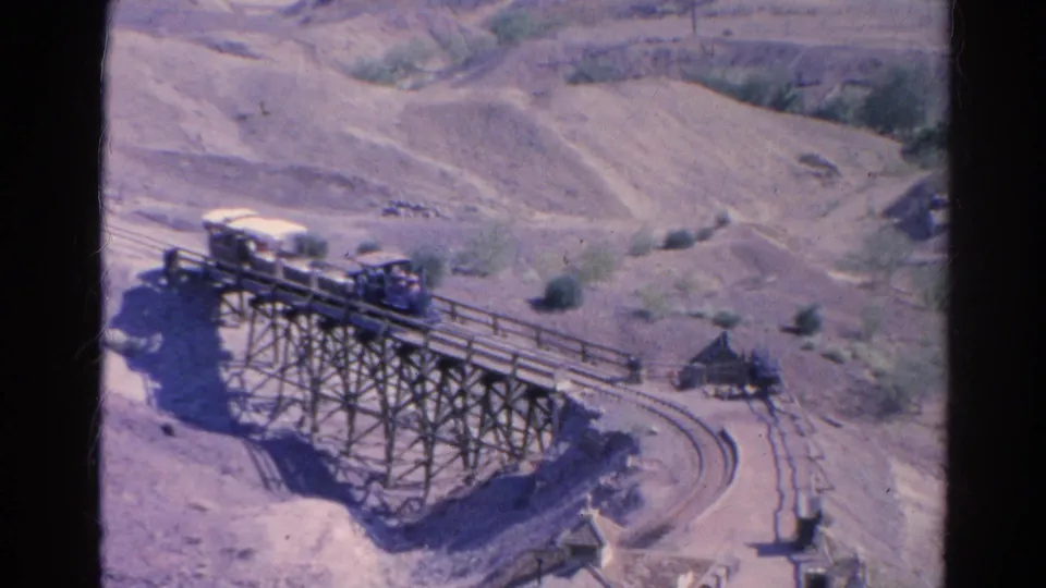 Small passenger train continues across the wooden trestle in 1966 Silver Lake, with scrubby hills behind it.