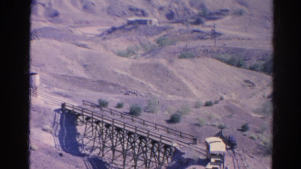 Wooden trestle bridge crossing a dry ravine in a pale desert hillside.
