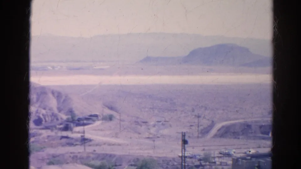 1966 Silver Lake, California 8mm frame showing a pale arid valley, distant hills, road grades, and utility lines.
