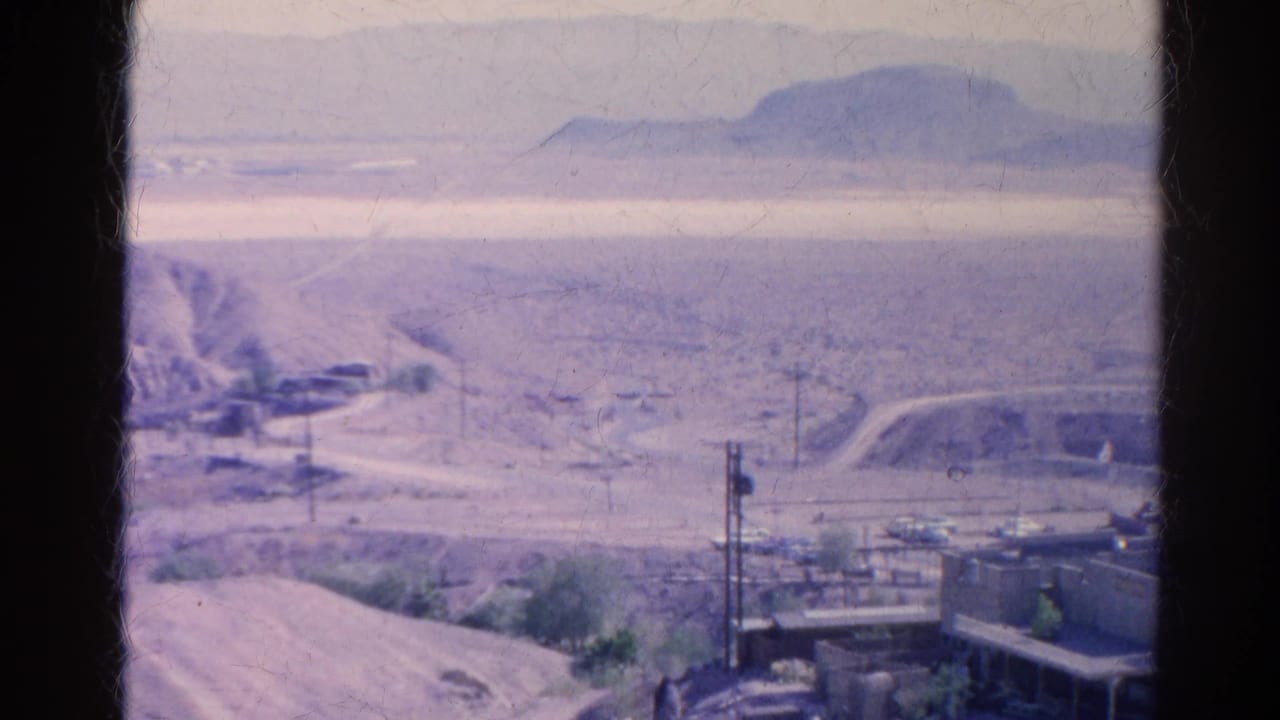 1966 Silver Lake, California 8mm frame overlooking desert infrastructure with a road, utility poles, vehicles, and a low ridge.