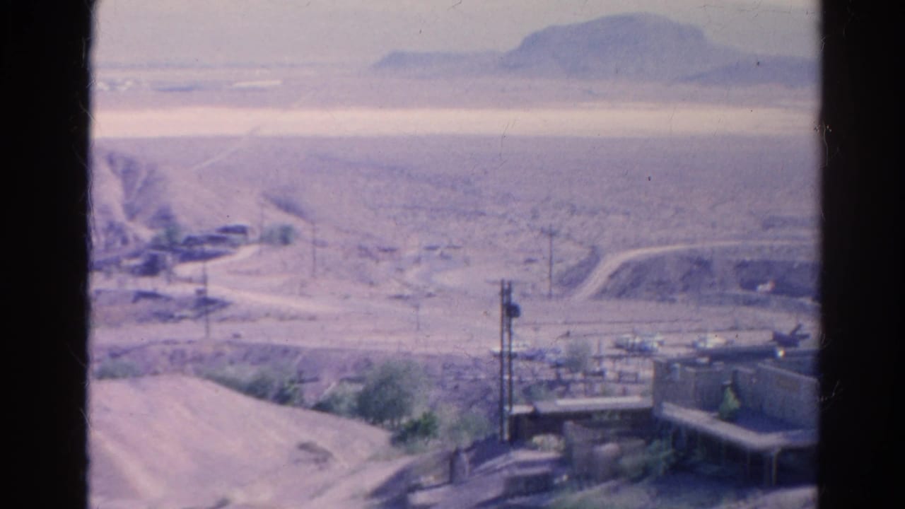 Desert buildings and utility poles seen across a hazy arid landscape.
