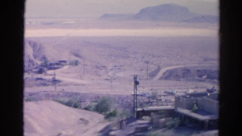 1966 home-movie frame looking over Silver Lake desert structures, utility poles, dirt roads, and distant hills under haze.