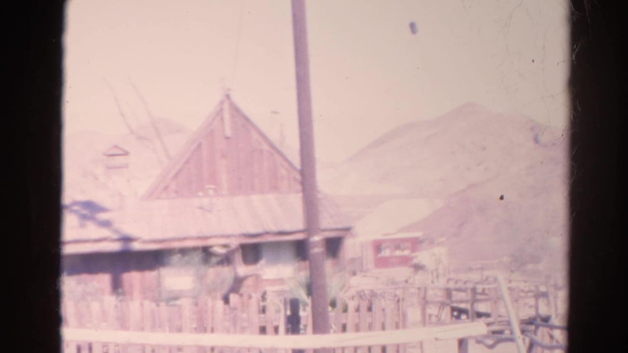 Weathered wooden building with a sloped roof, utility pole, fence, and dry hills behind it.