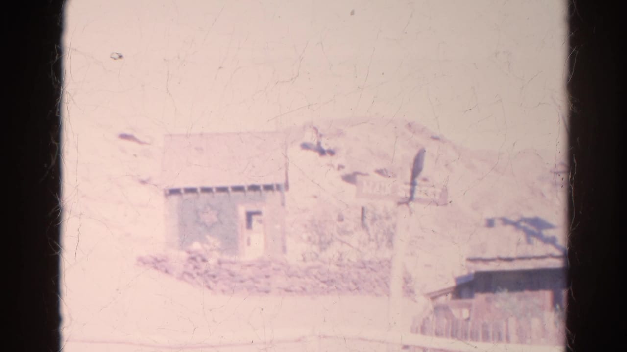 Final 1966 Silver Lake frame showing a pale small building, Main Street sign, partial roofline, fence, and dry hillside.