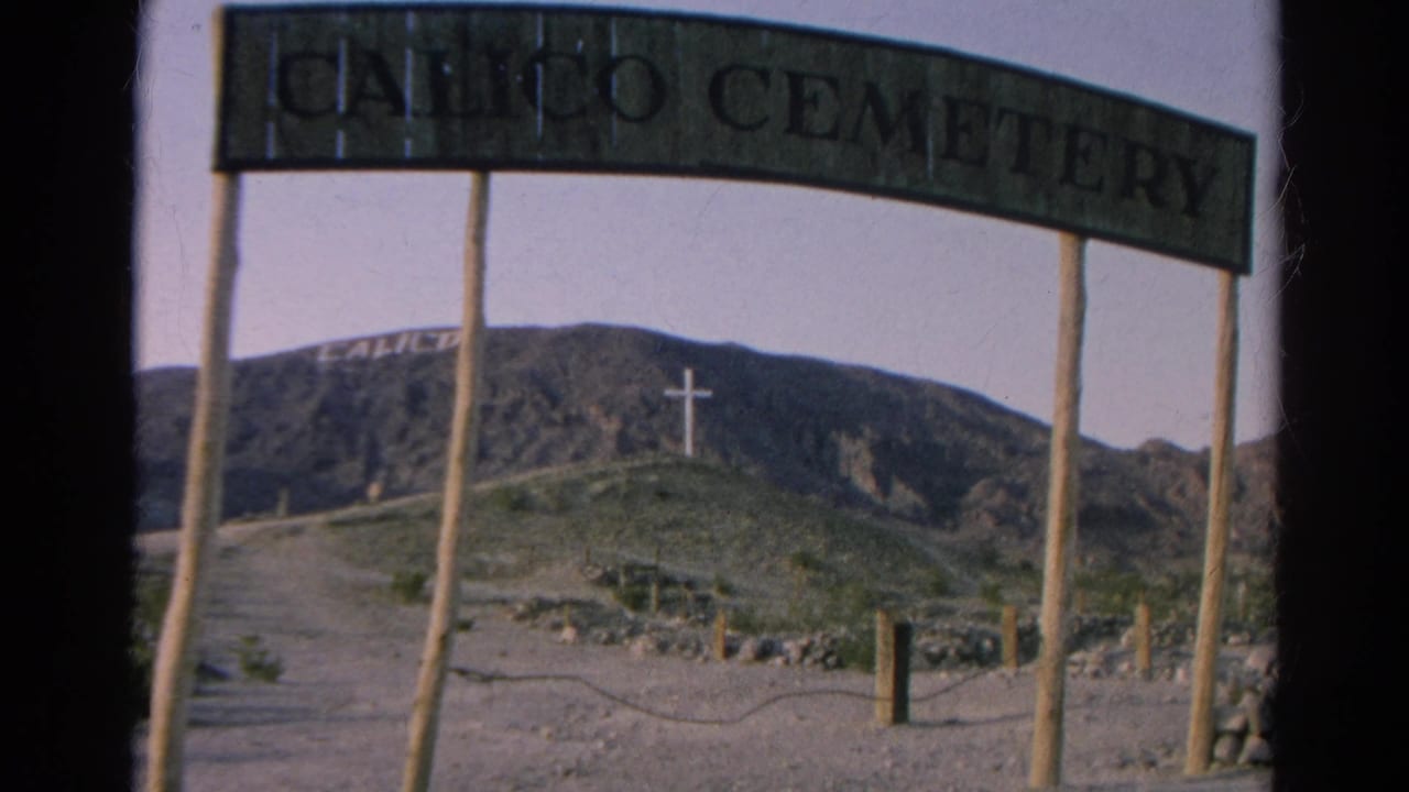 A visitor view of the Calico Cemetery entrance shows the arch sign, dirt road, hillside lettering, and distant white cross in 1966 California footage.