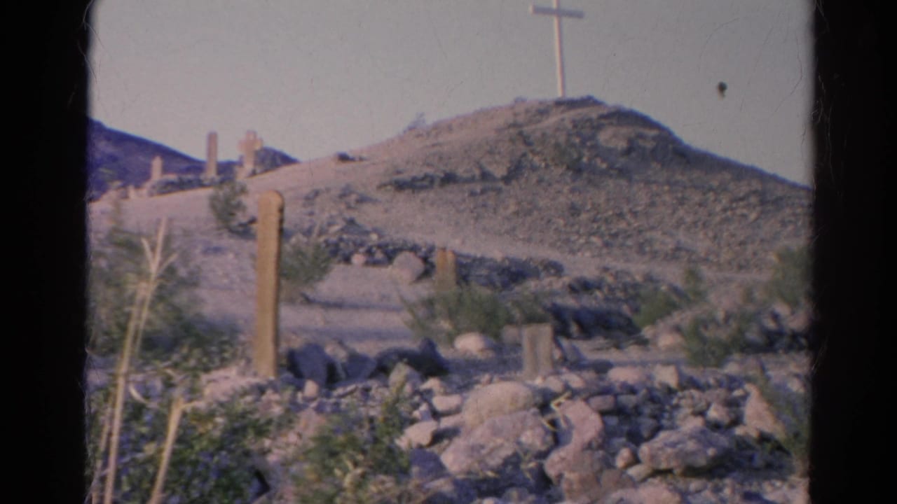 1966 8mm view of a rocky Silver Lake, California hillside with scattered desert plants, marker-like posts, and a white cross above the slope.