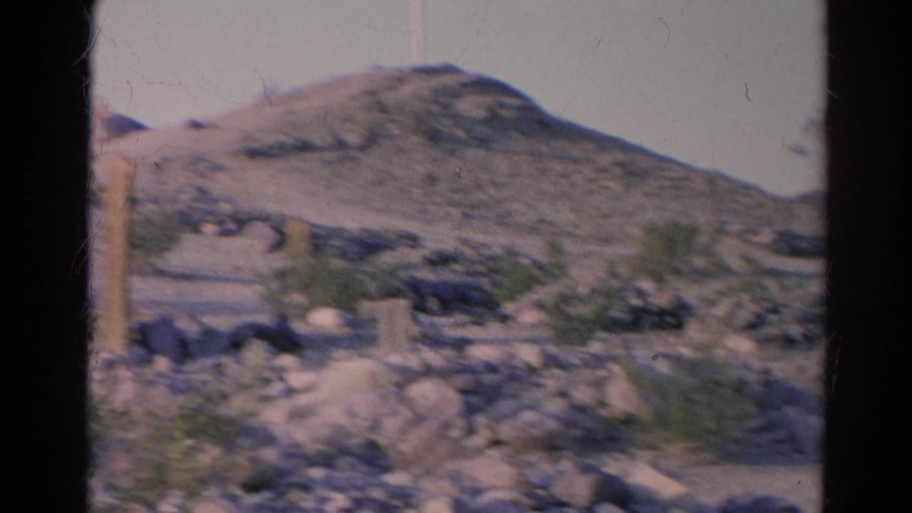Rocky slope and low hill with desert shrubs and dark gate borders from the film scan.