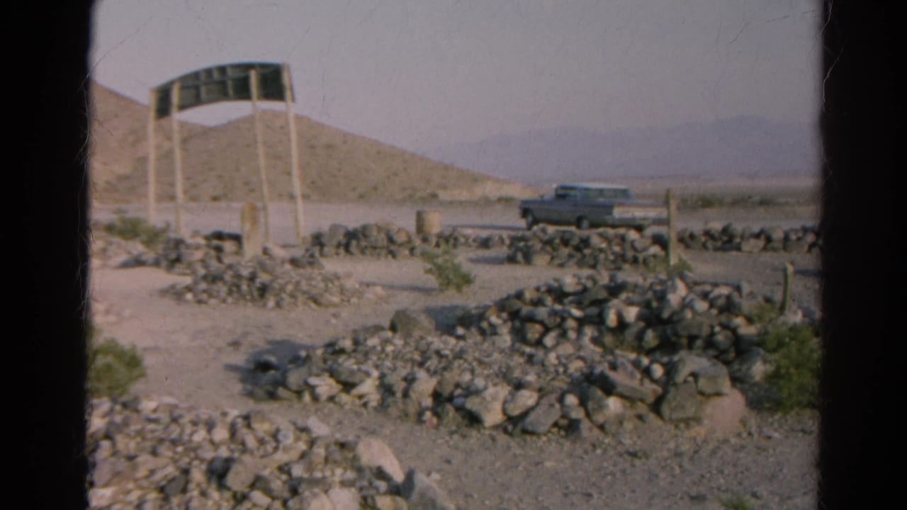 1966 8mm view near Silver Lake, California, showing a roadside sign, parked car, stone edging and arid hills.