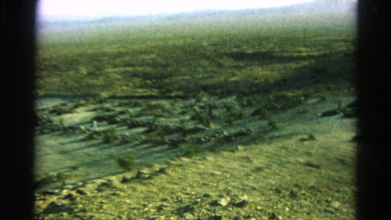 A 1966 Silver Lake, California 8mm view pans across dry terrain with scrub, dirt paths, distant hills, and visible frame borders.