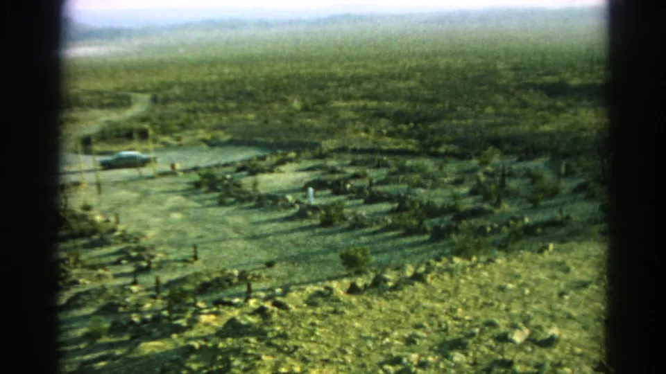1966 8mm roadside view in Silver Lake, California, showing a parked car near a dirt road, utility poles, scrub, and hazy hills.