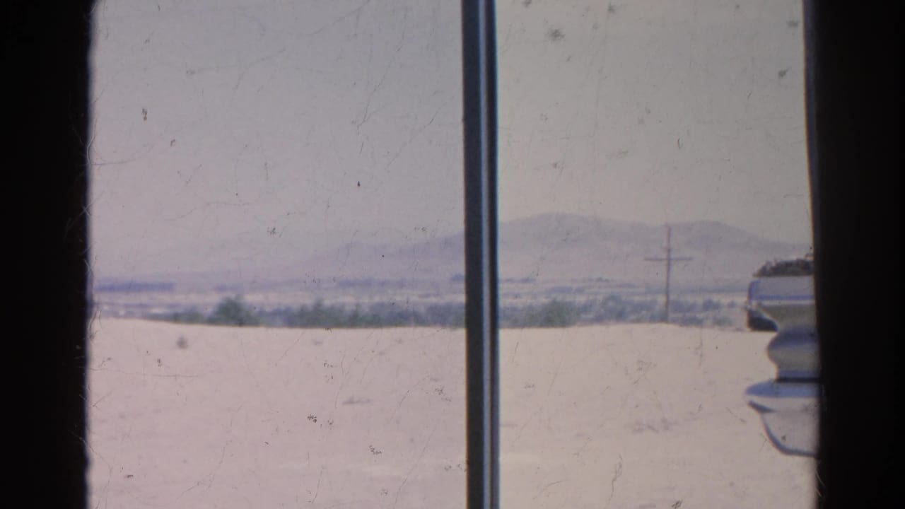 Arid landscape, distant hills, and a partial vehicle edge beyond a window frame.